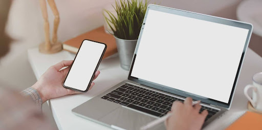 Uma mão esquerda segurando um celular enquanto a mão direita mexe no notebook