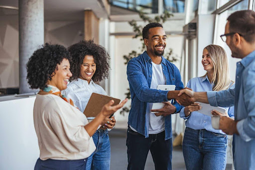 Grupo de pessoas se cumprimentando e sorrindo em local de trabalho
