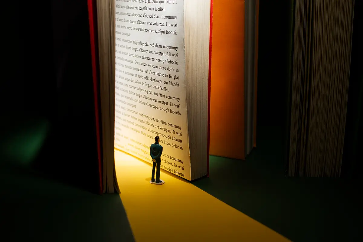 Colaborador em miniatura diante de um livro gigante, simbolizando o poder do storytelling na comunicação interna